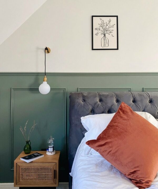 gold angler wall light installed on an off-white wall in a green and white panelled bedroom
