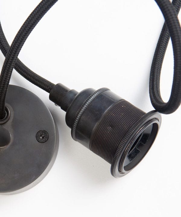 closeup of antique black bulb holder, fabric cable and ceiling rose against white background