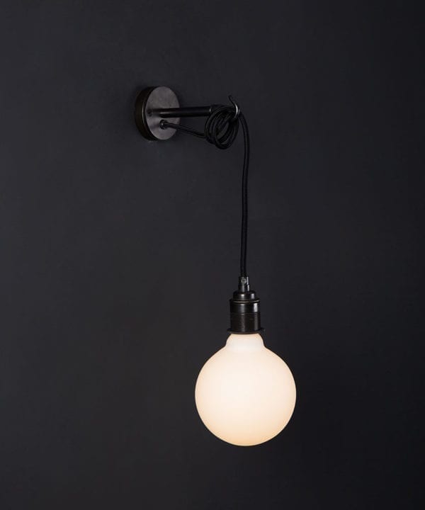 Black wall mounted light with lit opal bulb against a black wall