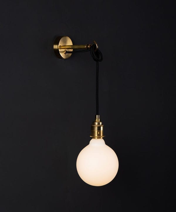 Brass wall mounted light with lit opal bulb against a black wall