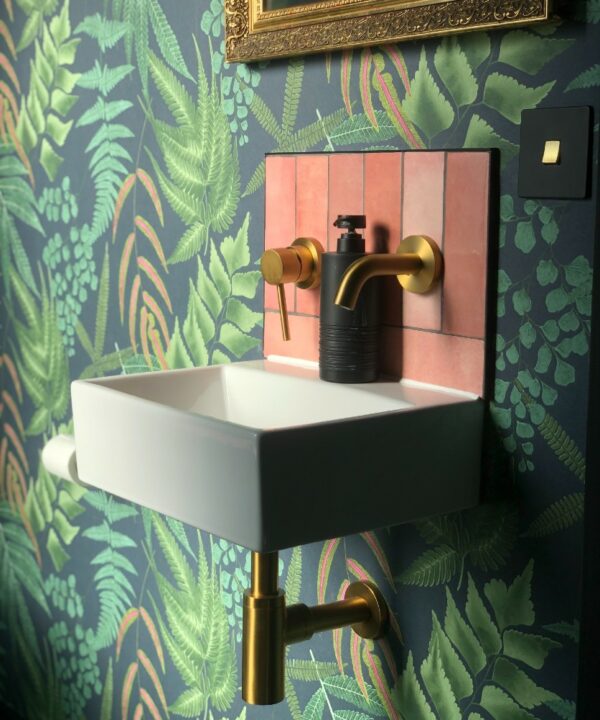 black and gold single rocker switch installed on a wall covered in patterned green wallpaper in a green and pink bathroom