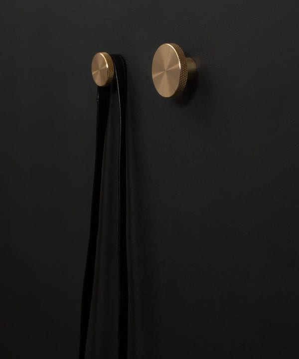 Modernist wall hook in gold attached to a black wall