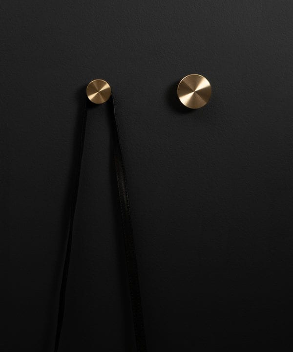 Modernist wall hook in gold attached to a black wall straight on shot