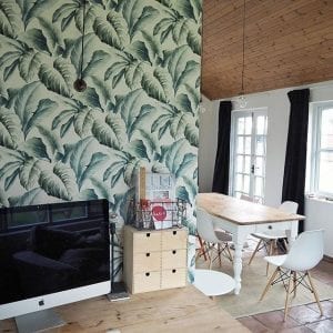 tropical print green wallpaper in an office space leading into white dining area with wooden cladded ceiling