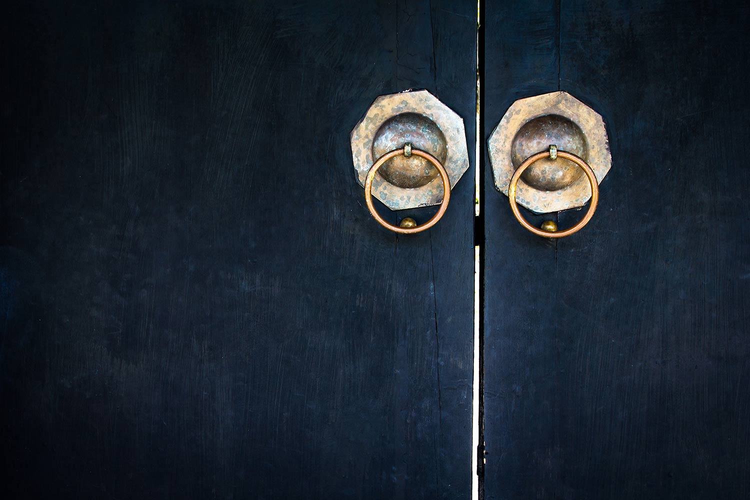 two brass door knockers on black wooden door