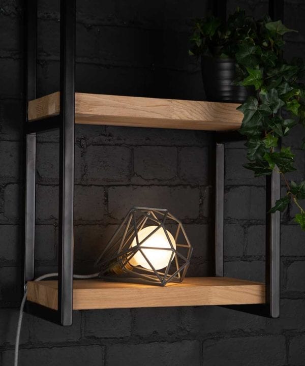 Grey cage shade table lamp on wooden shelf with frosted bulb switched on