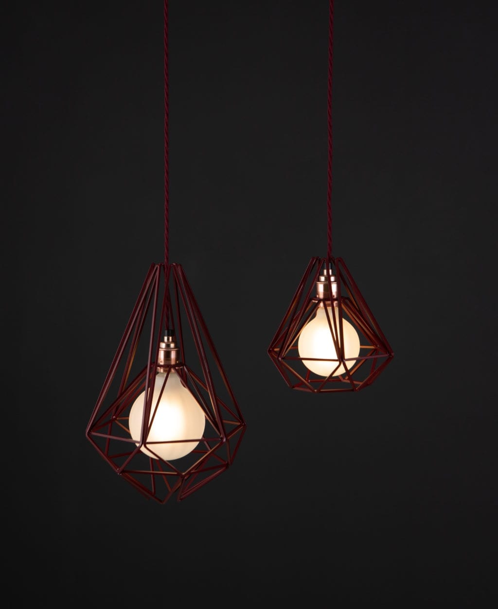 burgundy cage light with frosted bulbs suspended from burgundy twisted fabric cable against black background