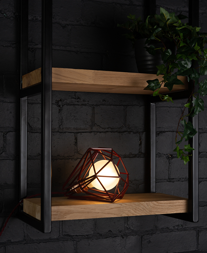 Burgundy cage shade table lamp on wooden shelf with frosted bulb switched on