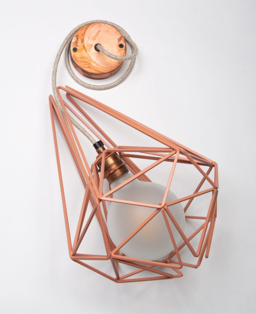 large pink metal cage pendant light with frosted bulb, linen fabric cable and tarnished copper bulb holder and ceiling rose against white background