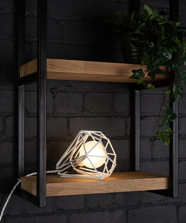 White cage shade table lamp on wooden shelf with frosted bulb switched on