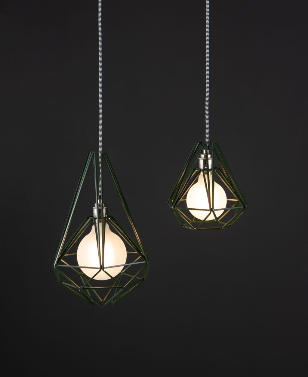 green metal cage light with frosted bulb suspended from black and white fabric cable against black background