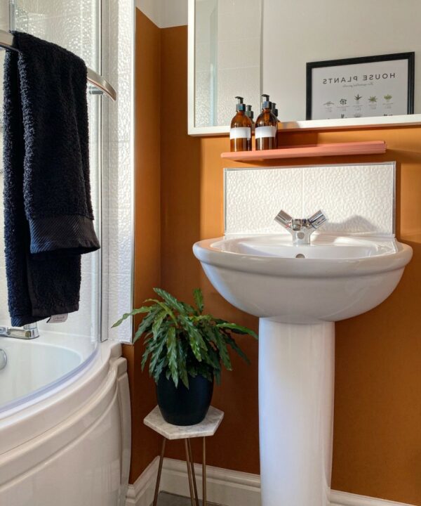 pink chai shelf installed on an orange wall above a sink in a white and orange bathroom