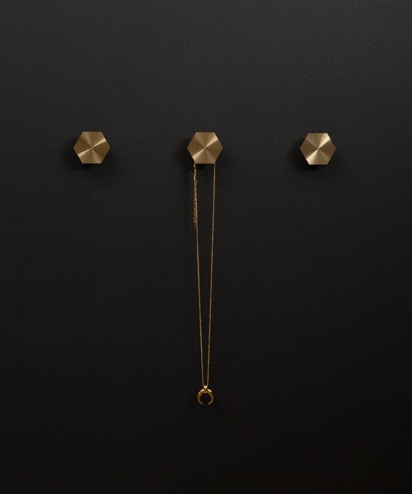 series of three bauhaus hexagonal modern coat hooks secured to a black wall straight on shot