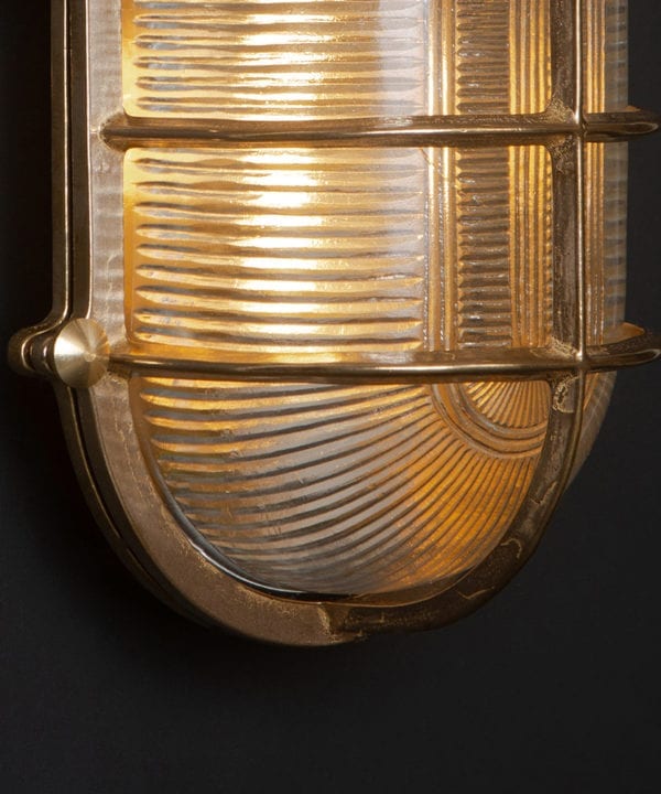 close up of lit big steve brass bulkhead wall light against black wall