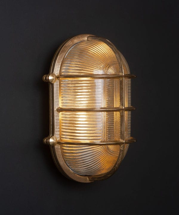 lit big steve brass bulkhead wall light against black wall