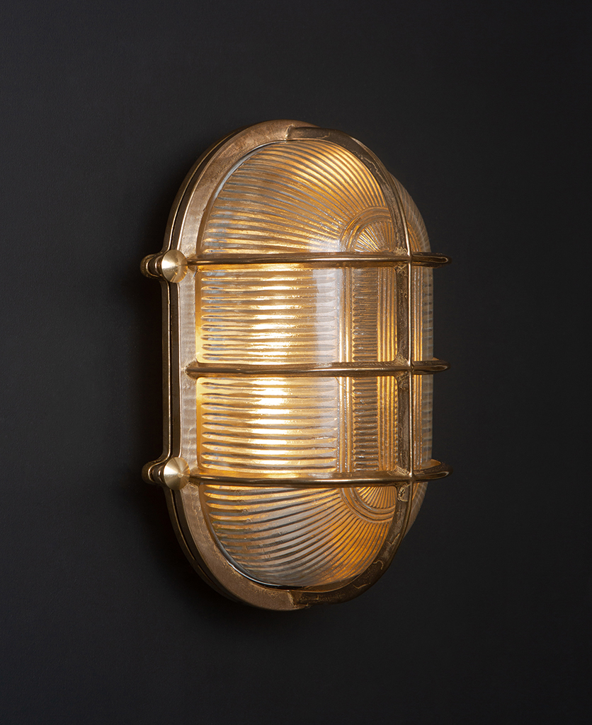 lit big steve brass bulkhead wall light against black wall