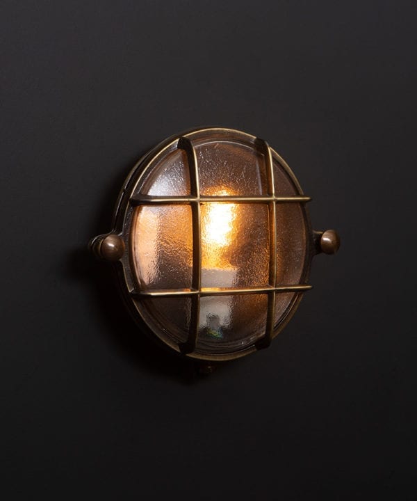 mark aged brass bulkhead light with lit bulb on black wall