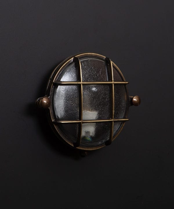 mark aged brass bulkhead light with unlit bulb on black wall