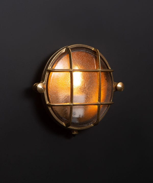 mark brass bulkhead light with lit bulb on black wall