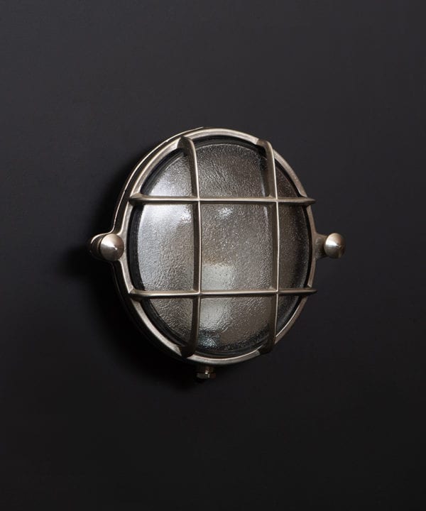 Mark silver bulkhead light with unlit bulb on black wall
