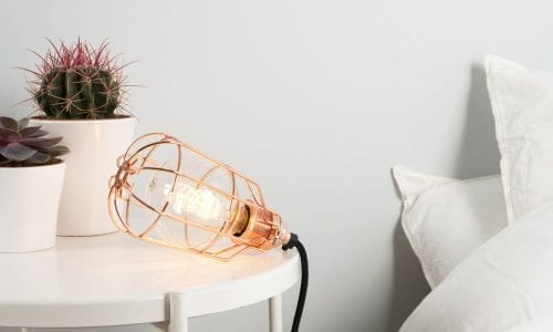 bedside table lamp featuring copper cage light shade, filament light bulb, copper bulb holder and black fabric lighting cable in a white bedroom