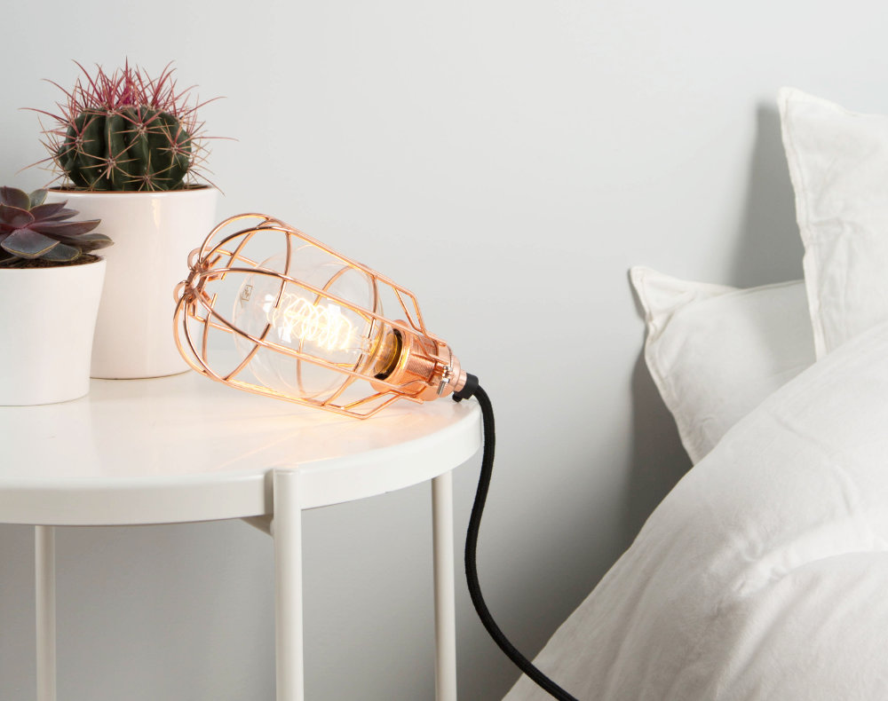 bedside table lamp featuring copper cage light shade, filament light bulb, copper bulb holder and black fabric lighting cable in a white bedroom