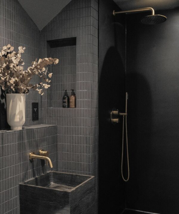 gold jadipai bathroom tap installed above a square grey sink in a dark grey tiled bathroom