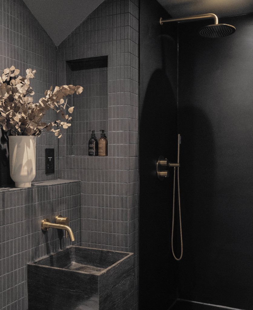 gold jadipai bathroom tap installed above a square grey sink in a dark grey tiled bathroom