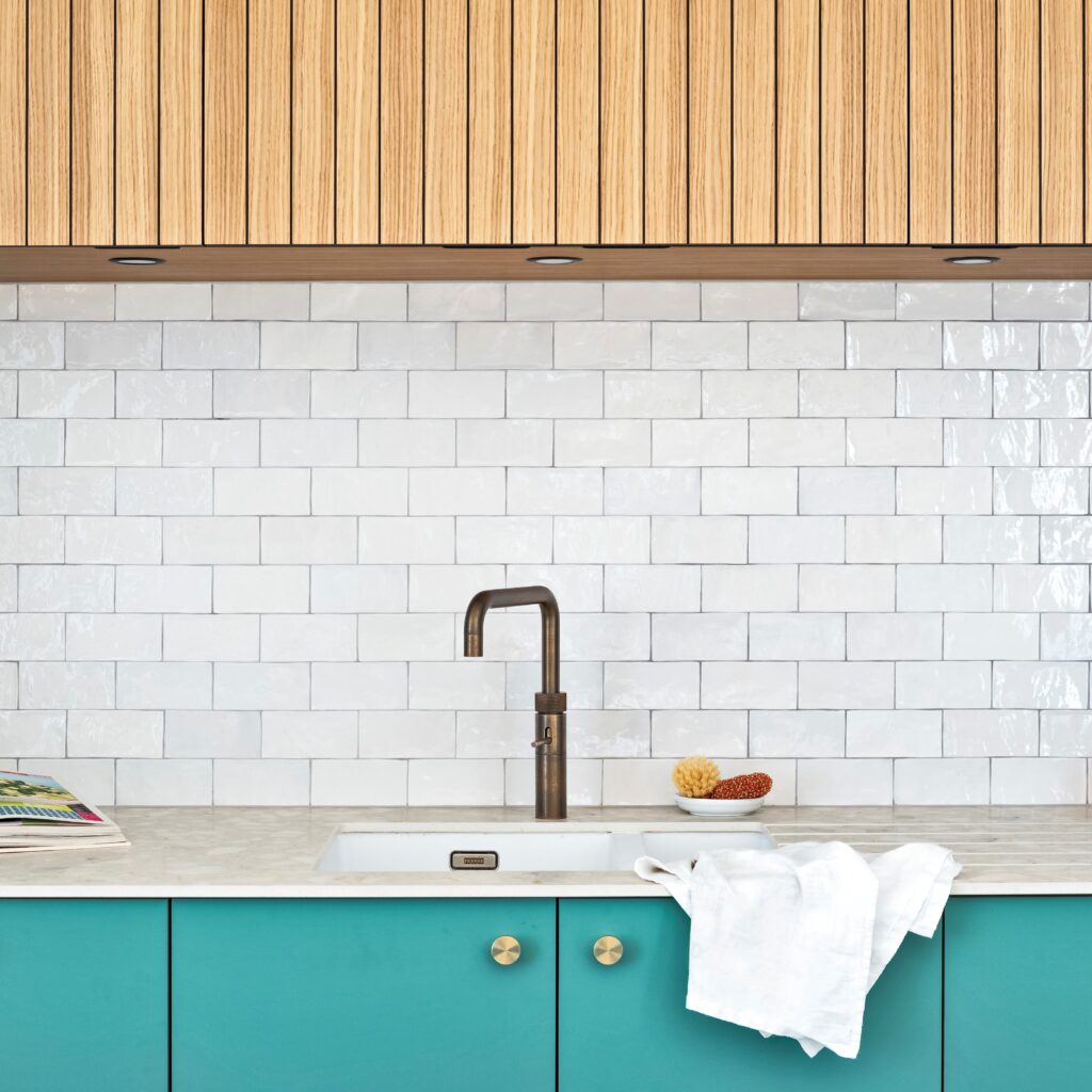 turquoise kitchen cabinets with gold knobs, marble worktop and white tiled wall with slatted wooden cupboards above