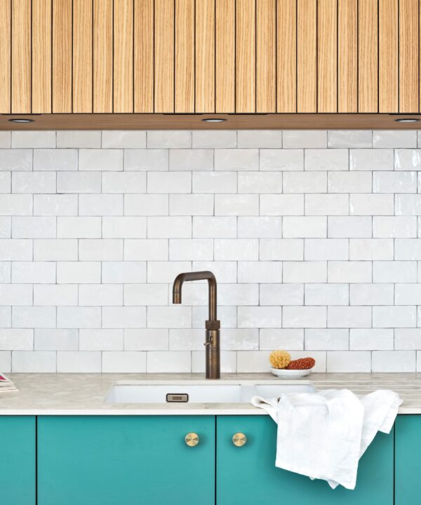 turquoise kitchen cabinets with gold knobs, marble worktop and white tiled wall with slatted wooden cupboards above