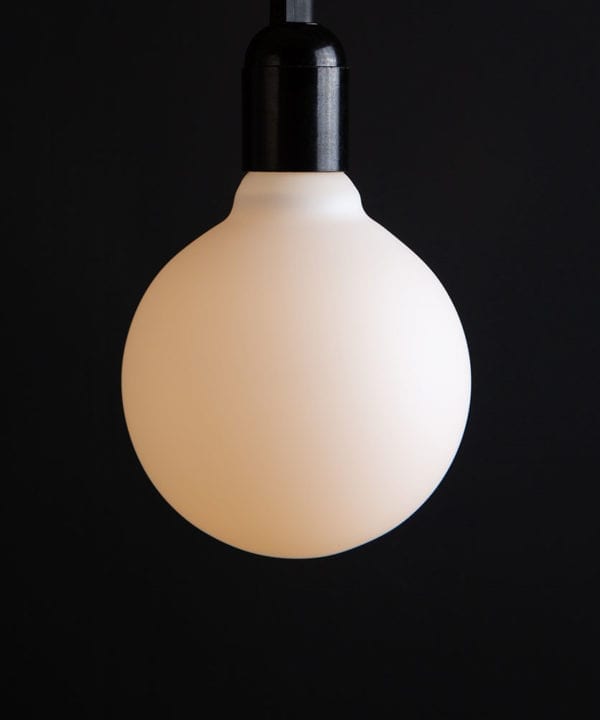 Lit Aurora decorative light bulbs suspended from bakelite bulb holder against black wall