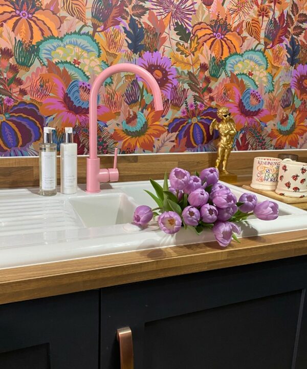 pink tinkisso tap on a white porcelai sink in front of some vibrant floral wallpaper in a kitchen