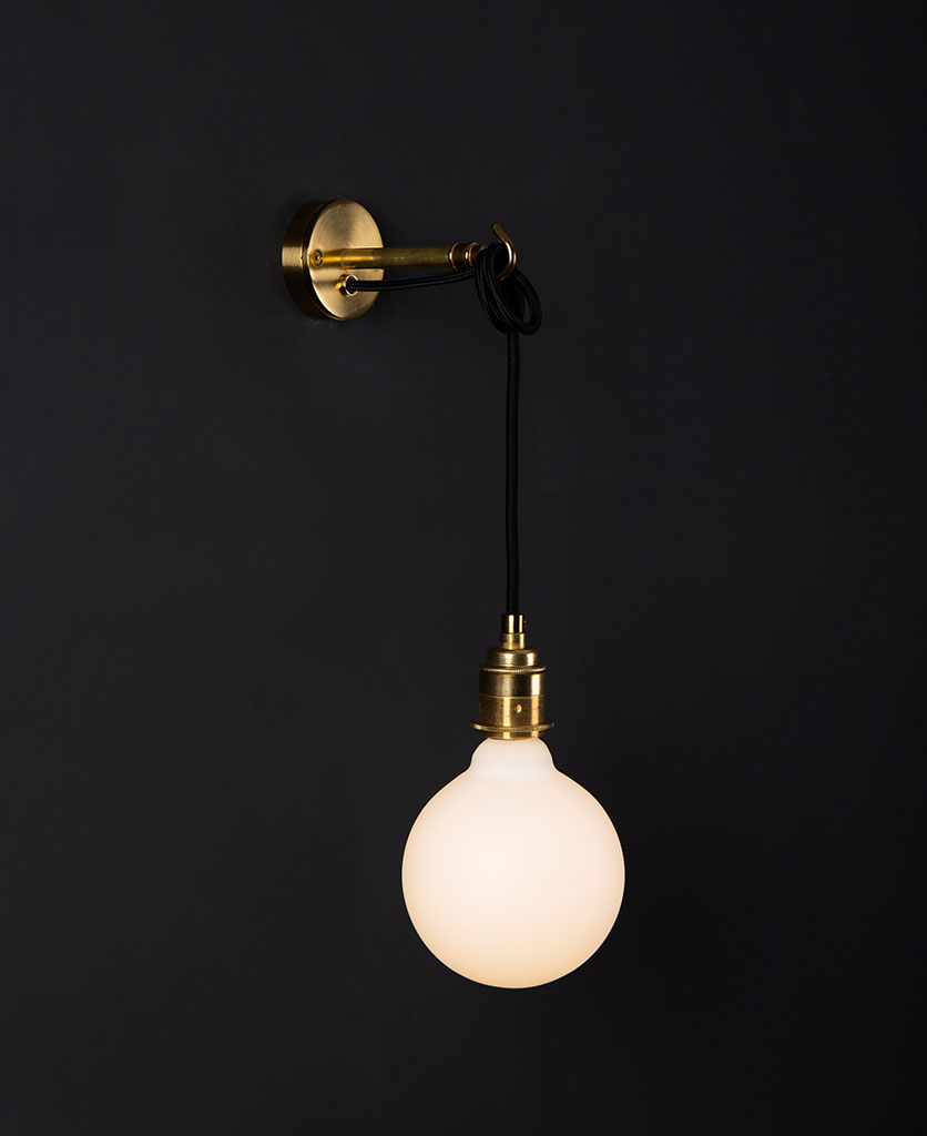 Brass wall mounted light with lit opal bulb against a black wall