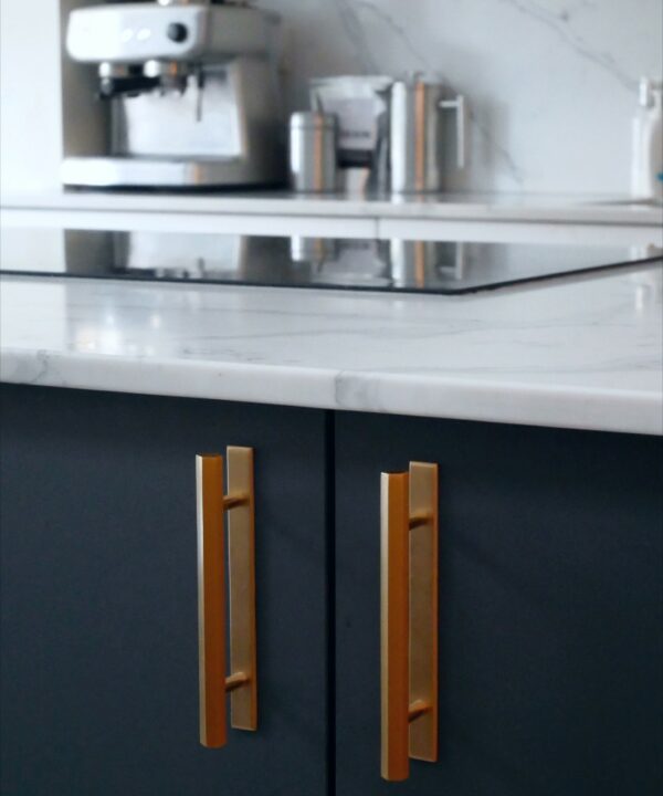 gold hive handes with plate installed on a dark grey cupboard in a white marble kitchen