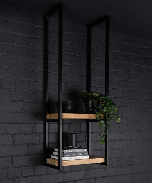 Knox steel shelves holding books and foliage against a black paintde brick wall