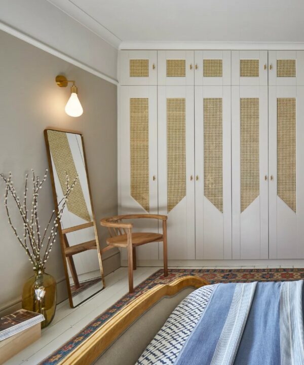 gold grosvenor wall light installed on an off white wall above a mirror in a bedroom