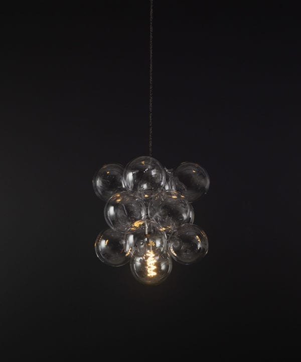 glass bubble light chandelier with 12 clear glass baubles and 1 bronze bulb holder suspended from textured fabric cable against a black wall