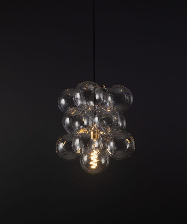 glass bubble light chandelier with 12 clear glass baubles and 1 gold bulb holder suspended from black fabric cable against a black wall