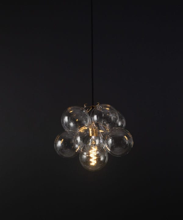 glass bubble light chandelier with 8 clear glass baubles and 1 gold bulb holder suspended from black fabric cable against a black wall