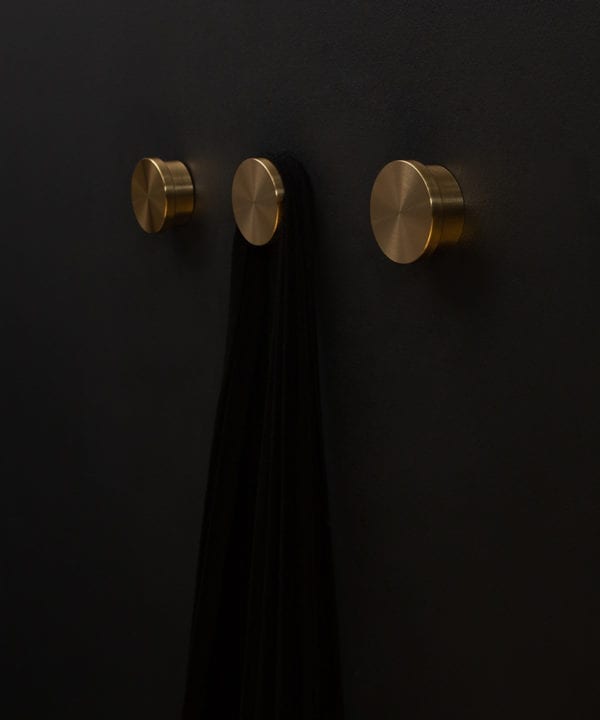 group of three gold baroque metal coat hooks on a black wall