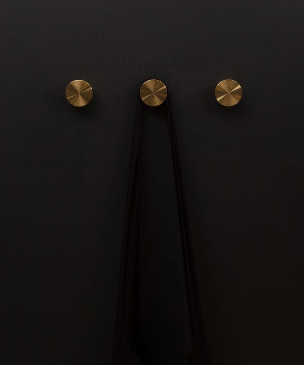 group of three gold baroque metal coat hooks on a black wall shot straight on