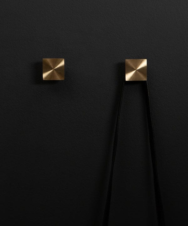 group of two expressionist wall coat hooks in brass on a black wall straight on shot