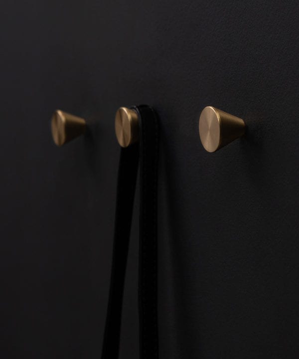 three futurist brass coat hooks on a black wall