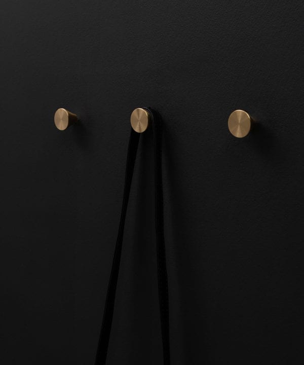 three futurist brass coat hooks on a black wall straight on shot