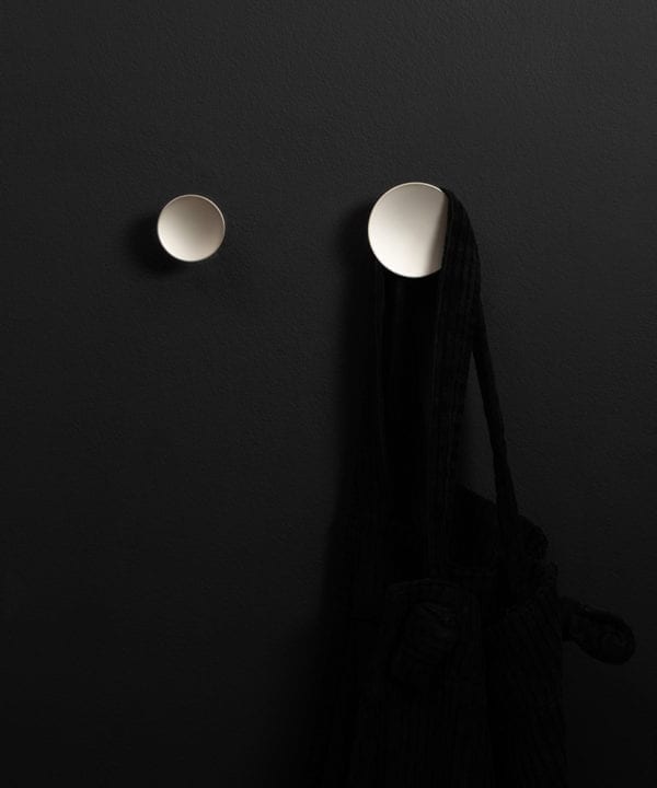 two silver Rococo kitchen hooks on a black wall shot straight on