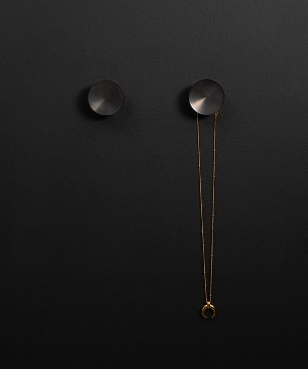 Surrealist coat hook attached to a black wall holding a gold necklace straight on shot