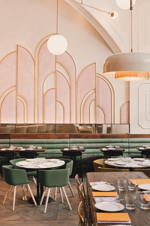 Art Deco style restaurant with sage green banquet seating and sweeping gold and pink arches on the walls