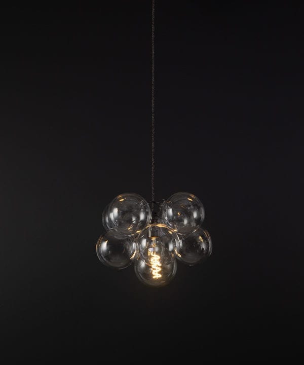 glass bubble light chandelier with 8 clear glass baubles and 1 bronze bulb holder suspended from textured fabric cable against a black wall