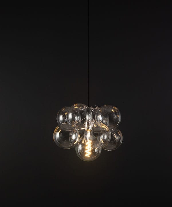 glass bubble light chandelier with 8 clear glass baubles and 1 silver bulb holder suspended from black fabric cable against a black wall