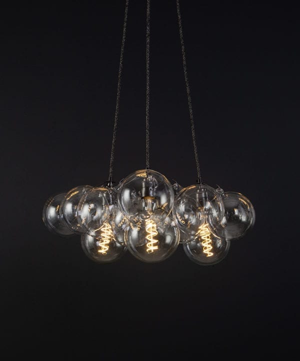 bubble pendant chandelier with 12 clear glass baubles and 3 bronze bulb holders suspended from textured fabric cable against a black wall